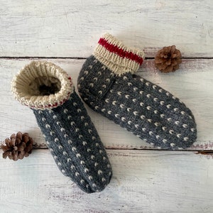 May include: A pair of cozy, hand-knitted gray slipper socks with white dot patterns. The cuffs are cream-colored with a red stripe. The socks are made of soft yarn, perfect for keeping feet warm. A rustic, handmade item.