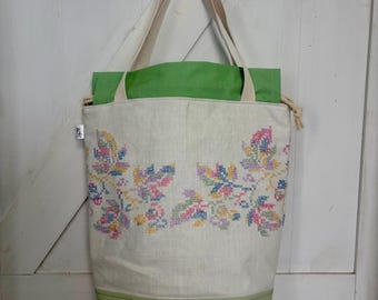 May include: A white tote bag with a green lining and a floral embroidery design. The bag has two handles and a green bottom.