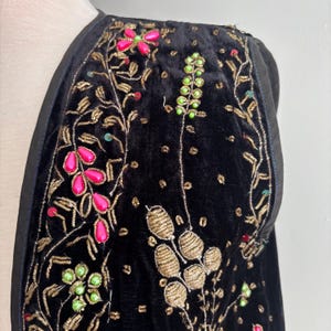 以下が含まれることがあります： 黒いベルベットのジャケット。金色の刺繍とピンクと緑のビーズのアクセントが施されています。 ジャケットは花柄と葉柄で、黒い革のトリムが付いています。 デザインは複雑で詳細で、豪華な外観を作り出しています。