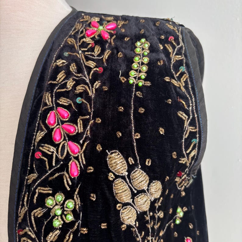 以下が含まれることがあります： 黒いベルベットのジャケット。金色の刺繍とピンクと緑のビーズのアクセントが施されています。 ジャケットは花柄と葉柄で、黒い革のトリムが付いています。 デザインは複雑で詳細で、豪華な外観を作り出しています。
