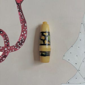 以下が含まれることがあります： 黒、緑、茶色の模様が施された、小さな黄色の指ぬき。 指ぬきは円筒形で、丸みを帯びた上部とわずかにフレアしたベースが付いています。 縫製に使用される可能性があります。