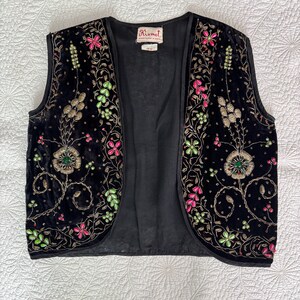 以下が含まれることがあります： ピンク、緑、金色の花の刺繍が施された黒いベルベットのベスト。ノースリーブのベストは丸いネックラインです。刺繍は詳細な花と葉が特徴です。ベストには「Kismet」と書かれたラベルが付いています。