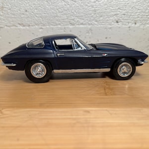 May include: A dark blue model car with silver rims and black tires. The classic coupe has a sleek design with a curved roof and is set on a wooden surface. The car is a miniature replica of a vintage vehicle.