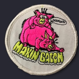 May include: Embroidered patch featuring two pink pigs, one atop the other, with the text "MAKIN' BACON" in yellow. The patch has a white border and a speech bubble that says "Ooooonk".