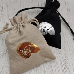 May include: Two small fabric drawstring bags with a nautilus shell design. One bag is beige with a gold shell and the other is black with a silver shell.