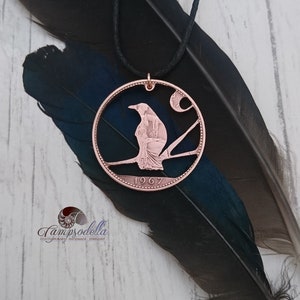May include: A copper-coloured coin pendant featuring a cut-out design of a bird perched on a branch with a crescent moon in the background. The coin is dated 1967.