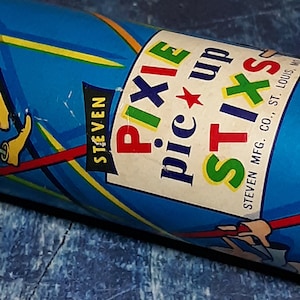 May include: A blue and white cardboard tube with the text "PIXIE pic up STIXS" and "STEVEN MFG. CO., ST. LOUIS, MO".