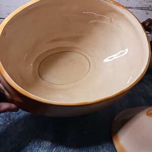 May include: A large, beige ceramic serving bowl with two handles. The bowl has a smooth, glossy finish and is empty.