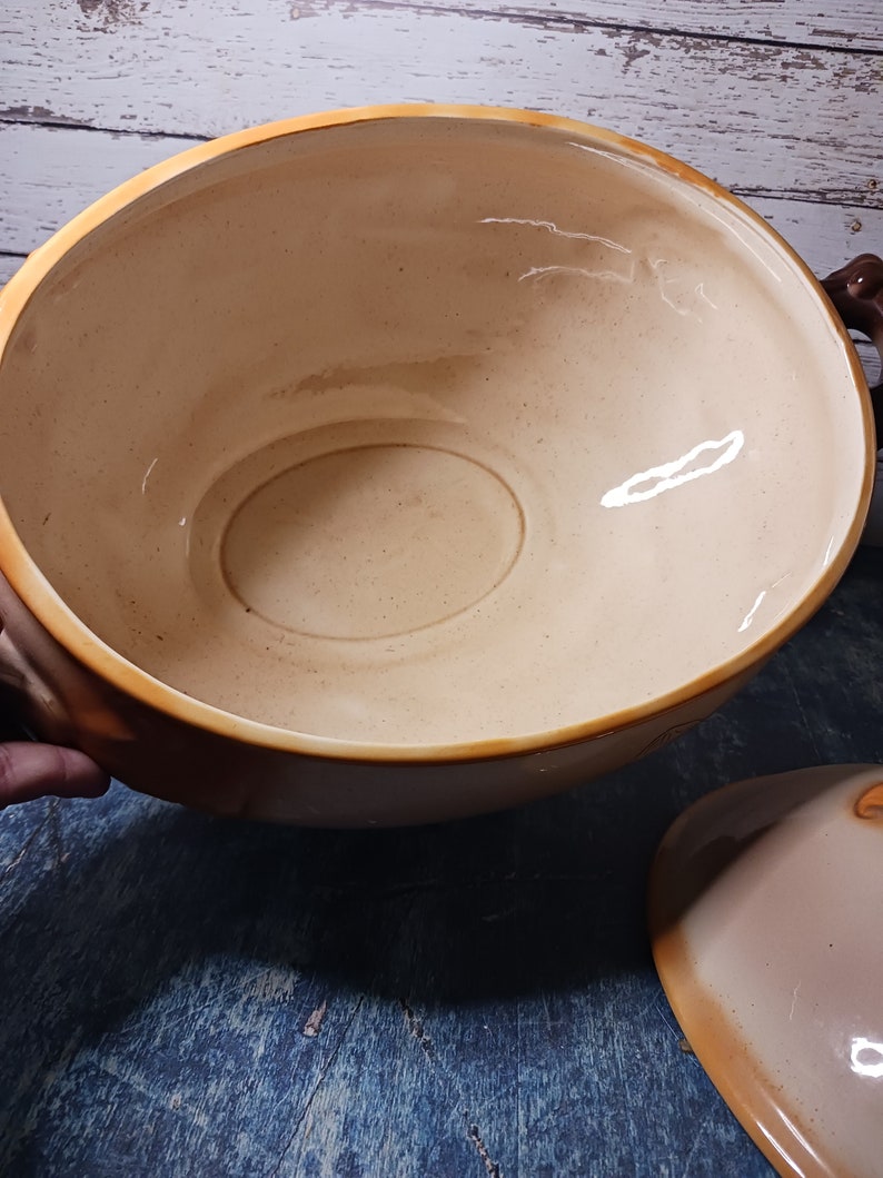 May include: A large, beige ceramic serving bowl with two handles. The bowl has a smooth, glossy finish and is empty.