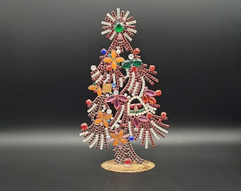 May include: A jeweled Christmas tree ornament with a gold base and red, green, orange, and white rhinestones.