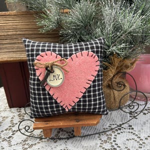 Peut inclure: Un petit coussin en tissu &agrave; carreaux noirs et blancs avec un c&oelig;ur en feutre rose cousu sur le devant. Le c&oelig;ur est orn&eacute; d'une cl&eacute; et d'une &eacute;tiquette sur laquelle est inscrit "Love". Le coussin est pos&eacute; sur un petit tra&icirc;neau en bois.