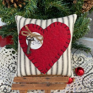Peut inclure: Un c&oelig;ur en feutre rouge avec une cl&eacute; et le mot "Love" sur un coussin &agrave; rayures blanches et noires. Le coussin est pos&eacute; sur un petit tra&icirc;neau en bois.