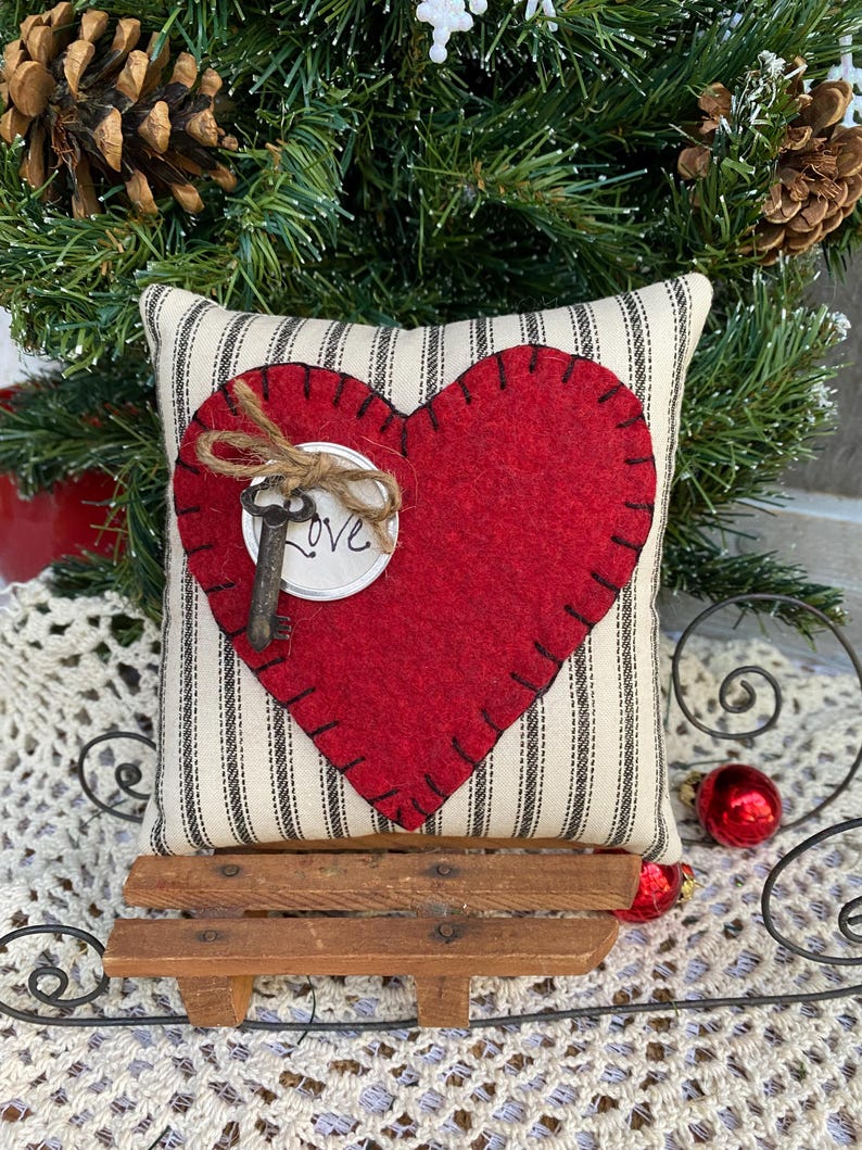 Peut inclure: Un c&oelig;ur en feutre rouge avec une cl&eacute; et le mot "Love" sur un coussin &agrave; rayures blanches et noires. Le coussin est pos&eacute; sur un petit tra&icirc;neau en bois.