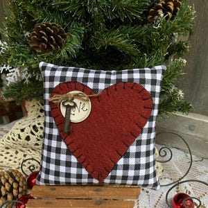 Peut inclure: Un coussin en forme de c&oelig;ur en feutre rouge avec une cl&eacute; et le mot "Love" sur un coussin &agrave; carreaux noirs et blancs. Le coussin est pos&eacute; sur un tra&icirc;neau en bois.