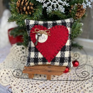 Peut inclure: Un coussin &agrave; carreaux noirs et blancs avec un c&oelig;ur en feutre rouge et une cl&eacute; avec une &eacute;tiquette "Love". Le coussin est pos&eacute; sur un petit banc en bois.