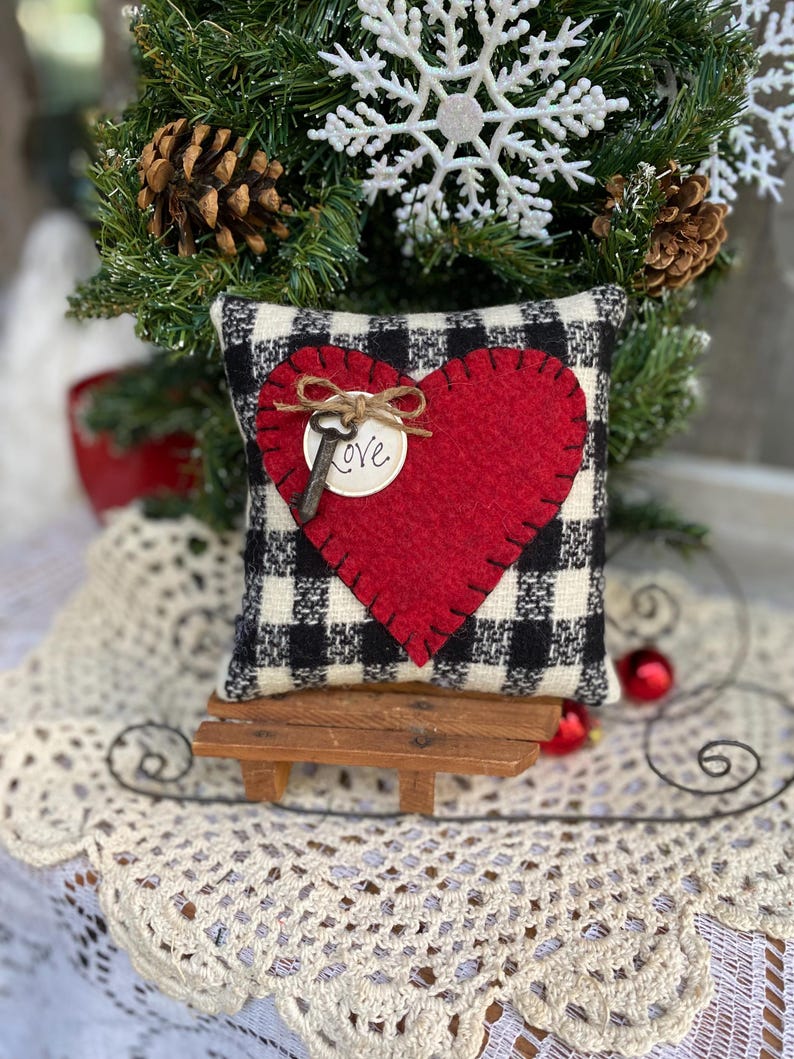 Peut inclure: Un coussin &agrave; carreaux noirs et blancs avec un c&oelig;ur en feutre rouge et une cl&eacute; avec une &eacute;tiquette "Love". Le coussin est pos&eacute; sur un petit banc en bois.