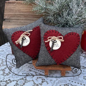 Peut inclure: Deux coussins en forme de c&oelig;ur gris et rouge avec une cl&eacute; et le mot "Love" sur chacun. Les coussins sont pos&eacute;s sur un tra&icirc;neau en bois.