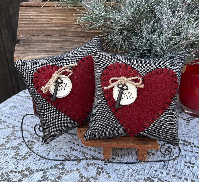 Peut inclure: Deux coussins en forme de c&oelig;ur gris et rouge avec une cl&eacute; et le mot "Love" sur chacun. Les coussins sont pos&eacute;s sur un tra&icirc;neau en bois.