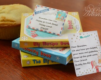May include: A stack of children's books titled "Elf Recipe Book" and "Coloring Book" with an "Elf Mail" envelope and a note from "Buddy the Elf". A yellow cupcake is in the background.