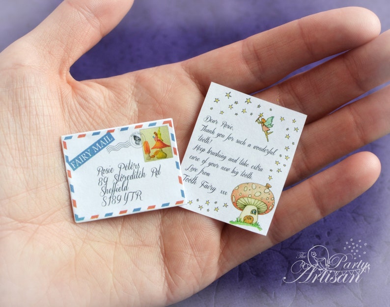 Może przedstawiać: Miniaturowa koperta i list z wr&oacute;żkową pocztą. Koperta jest biała z niebieskimi i czerwonymi obramowaniami oraz napisem "FAIRY MAIL". List zawiera ilustrację wr&oacute;żki i tekst "Droga Rose, Dziękuję za tak wspaniały ząb!"