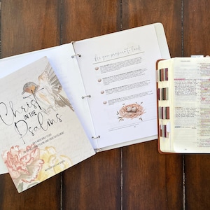 Könnte beinhalten: Ein weißer Ordner mit dem Text "As you prepare to lead!" und einer Aquarell-Illustration eines Vogelnests mit Eiern. Ein weißes Buch mit dem Titel "Christ in the Psalms" und einer Aquarell-Illustration eines Vogels. Eine braune, ledergebundene Bibel mit einem Lesezeichen und hervorgehobenem Text.