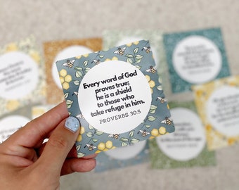 May include: A blue and yellow card with a beehive pattern and a white circle containing the text "Every word of God proves true; he is a shield to those who take refuge in him. Proverbs 30:5"