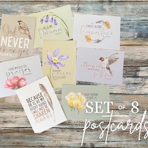 May include: A set of eight postcards with watercolor illustrations and inspirational quotes. The cards feature images of birds, flowers, and feathers, with text from Psalms. The words "God Never Changes" and "Set of 8 Postcards" are visible.