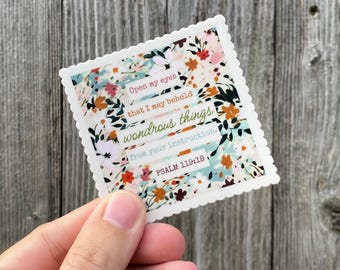 May include: A square sticker with a floral design in shades of pink, orange, and blue. The sticker has a scalloped edge and features the text "Open my eyes that I may behold wondrous things from your instruction. Psalm 119:18."