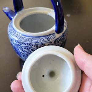 May include: A blue and white porcelain teapot with a lid. The teapot has a floral design and a blue handle. The lid has a small hole in the center.