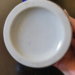 May include: The bottom of a blue and white ceramic teapot with a white glaze. The teapot has a blue floral design.