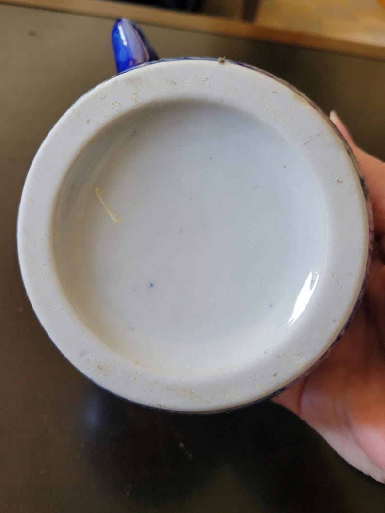 May include: The bottom of a blue and white ceramic teapot with a white glaze. The teapot has a blue floral design.