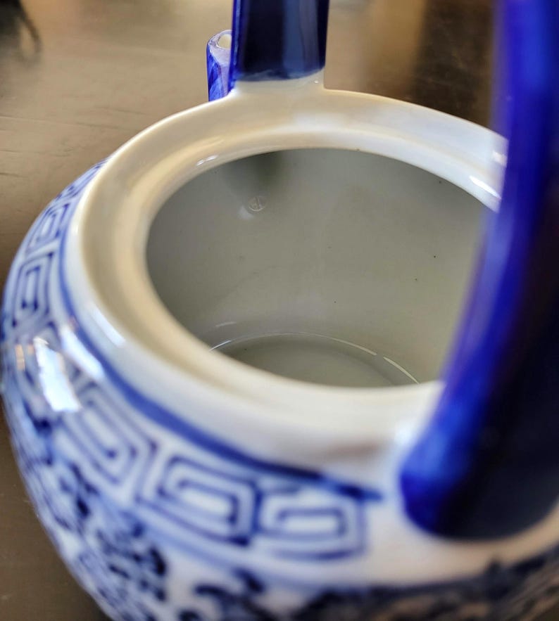 May include: Blue and white porcelain teapot with a blue handle. The teapot has a traditional Chinese design with a geometric pattern and floral motifs. The inside of the teapot is white.