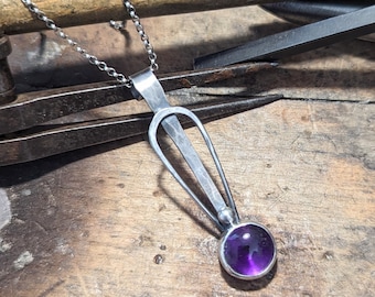 May include: A silver pendant necklace with a purple gemstone. The pendant is shaped like a teardrop with a small round gemstone at the bottom.
