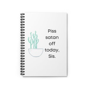 May include: A white spiral notebook with the text "Piss satan off today, Sis." printed in black. A green cactus plant is illustrated in a white pot.