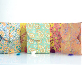 May include: Five colorful patterned gift bags with gold string ties and tassels. The bags are arranged in a row from left to right. The bags are made of paper and have a variety of floral and paisley designs.