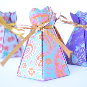 May include: Three small, pyramid-shaped gift boxes with gold ribbon. The boxes are made of paper with a floral pattern. The boxes are blue, purple, and pink.