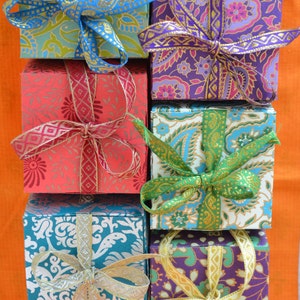 May include: Six small, square gift boxes with colorful patterned paper and tied with ribbon bows. The boxes are stacked in a pyramid shape. The boxes are decorated with different colors and patterns, including blue, green, purple, red, and gold.