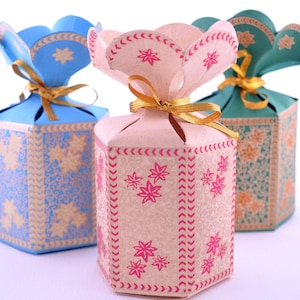 May include: Three hexagonal gift boxes in blue, pink, and teal, each with a floral design and a petal-shaped top tied with a gold ribbon. The boxes have a decorative pattern and are suitable for small gifts.
