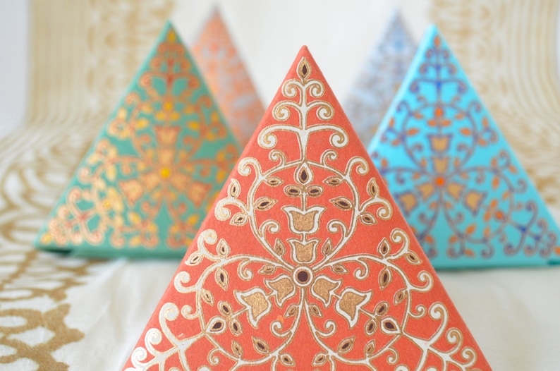 May include: Three decorative pyramid-shaped boxes with intricate floral patterns. The boxes are in shades of teal, blue, and coral with gold accents.