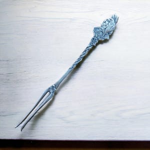 May include: A silver fork with a decorative handle featuring a detailed human face and floral design.