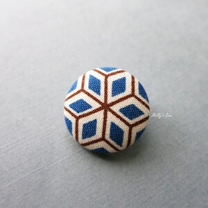 May include: A round, blue and brown fabric button with a geometric pattern. The button is about 1 inch in diameter.