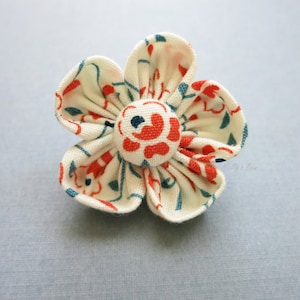 以下が含まれることがあります： 赤と青の花柄の白い布の花。花の中心は白い花柄の赤いボタンです。