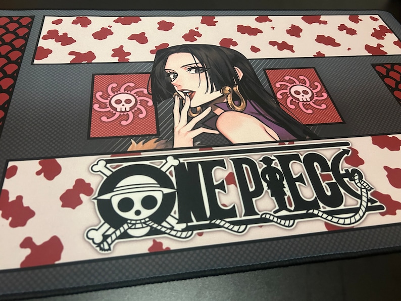 Puede incluir: Un rat&oacute;n de ordenador One Piece en blanco y negro con un fondo de estampado de vaca rojo y blanco. El rat&oacute;n de ordenador presenta una ilustraci&oacute;n en blanco y negro del logotipo de One Piece y un personaje de la serie de anime.