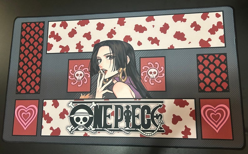 Puede incluir: Un logotipo "One Piece" en blanco y negro con una calavera y huesos cruzados sobre un fondo gris. El logotipo est&aacute; rodeado de un patr&oacute;n de estampado de vaca rojo y blanco. Una mujer con el pelo largo y negro y un vestido morado est&aacute; en el fondo.