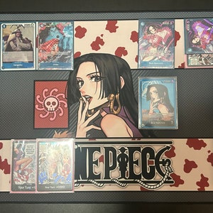 Puede incluir: Un tapete de juego de cartas coleccionables de One Piece con una ilustraci&oacute;n en blanco y negro de una mujer con cabello negro largo y un s&iacute;mbolo de calavera y huesos cruzados. El tapete de juego tiene un fondo de estampado de vaca rojo y blanco con las palabras "One Piece" en negro.