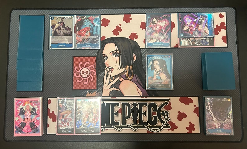 Puede incluir: Un tapete de juego de cartas coleccionables de One Piece con una ilustraci&oacute;n en blanco y negro de una mujer con cabello negro largo y un s&iacute;mbolo de calavera y huesos cruzados. El tapete de juego tiene un fondo de estampado de vaca rojo y blanco con las palabras "One Piece" en negro.