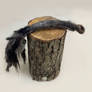 Może przedstawiać: Długi, ciemnoszary i biały kawałek przędzy leży na drewnianym kłodzie. Przędza jest fakturowana i wydaje się być przędziona ręcznie.