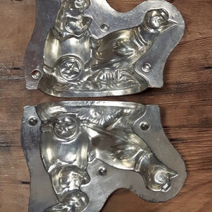 May include: Two vintage metal molds for making chocolate candy. The molds are shaped like a rabbit and a bird. The molds are made of silver-colored metal and have a detailed design.