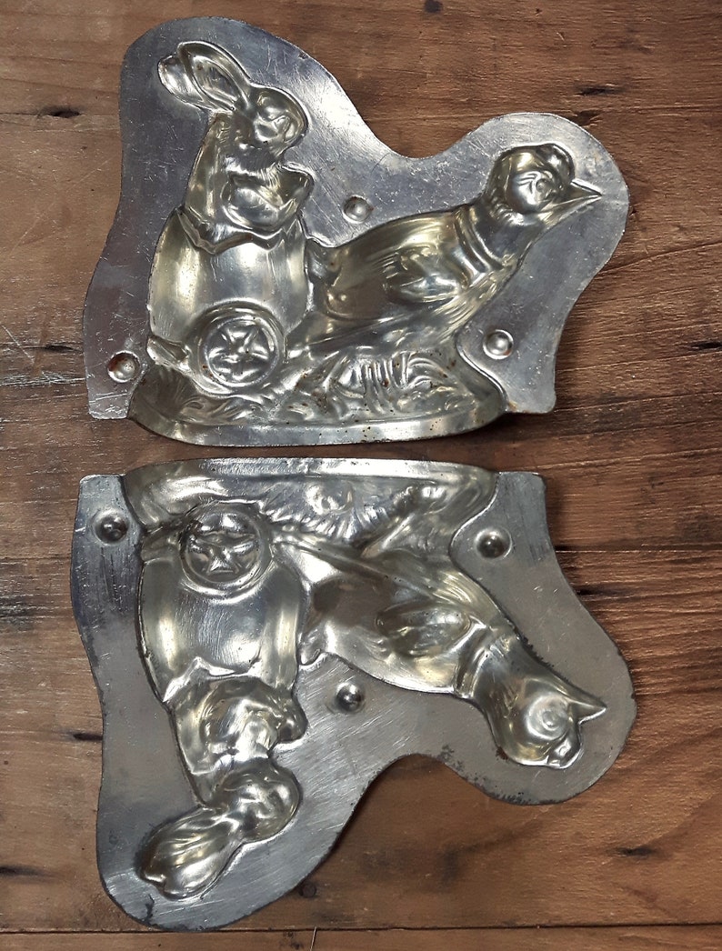 May include: Two vintage metal molds for making chocolate candy. The molds are shaped like a rabbit and a bird. The molds are made of silver-colored metal and have a detailed design.