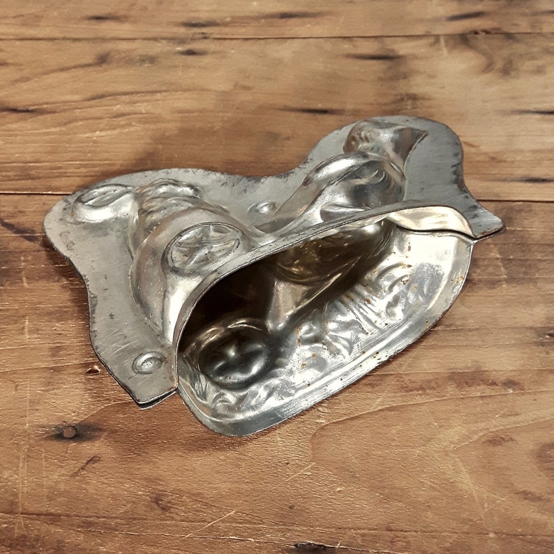 May include: A vintage metal mold for making chocolate candy. The mold is shaped like a person riding a bicycle. The mold is silver in color and has a worn, antique look.